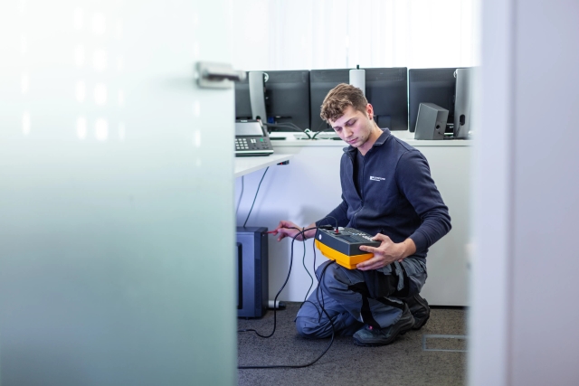 Ein Mitarbeiter von VD-Elektrotechnik arbeitet an einem rechner mit einem Messgerät. Er prüft die Stromstärken.